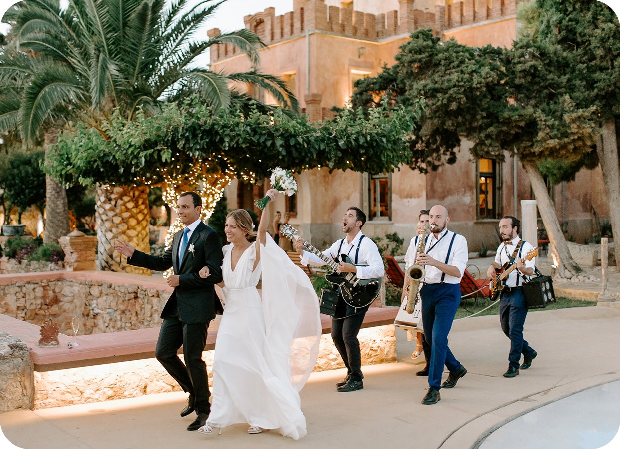 The couple and the band walking through the gardens at golden hour