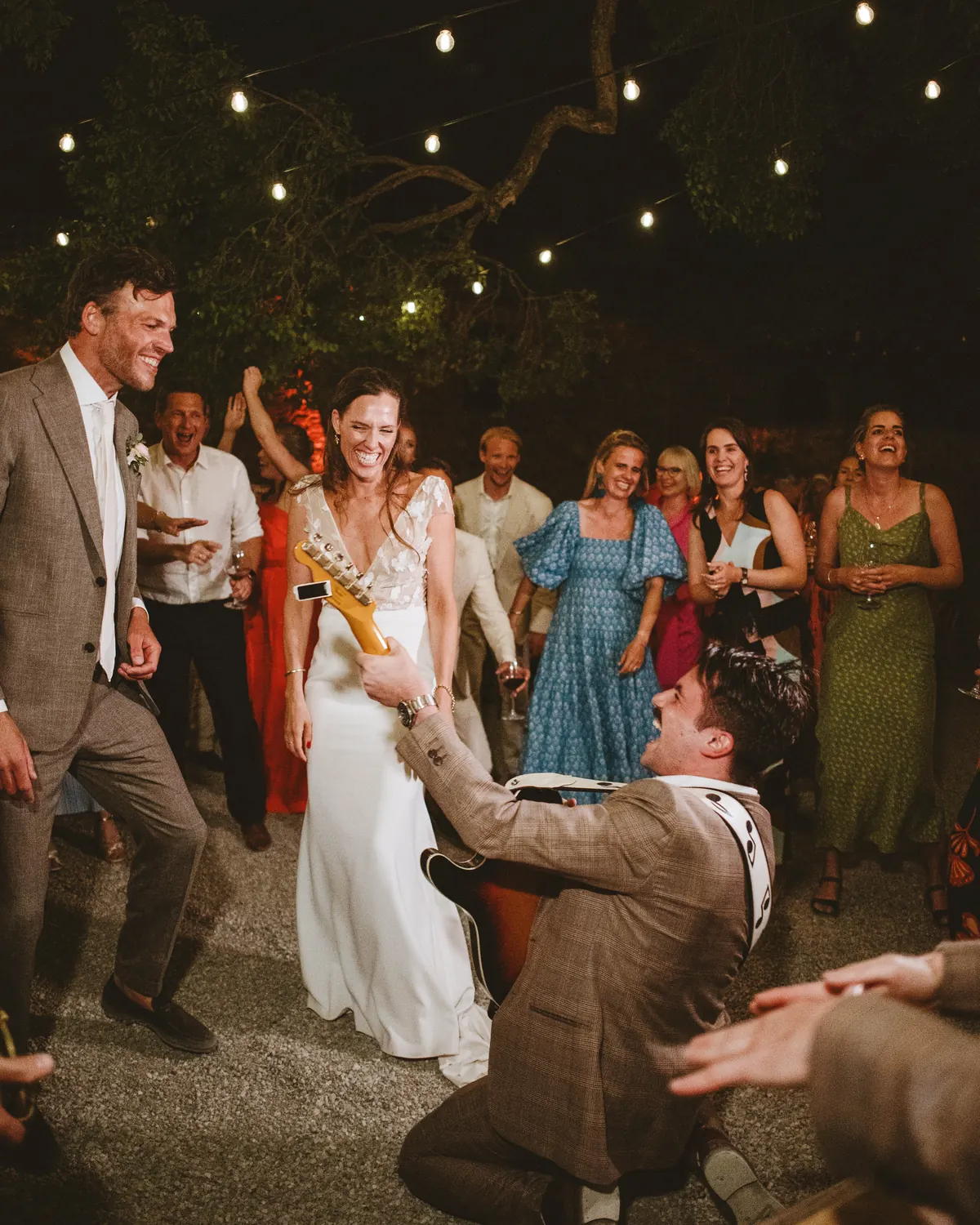 The bride dancing with the band as a guest kneels in front of her under string lights
